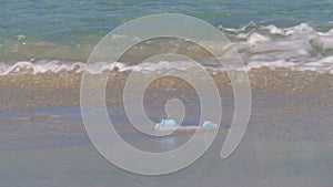 Woman cleans up a used face mask on the beach. People pollute the ocean