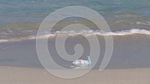 Woman cleans up a used face mask on the beach. Pollution of nature by people