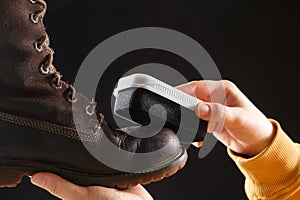 The woman cleanses and applies the cream to brown nubuck women& x27;s winter boots with a sponge. On a black background