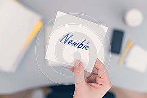 Woman clerk sitting holding note paper sticker with newbie word. Business concept.