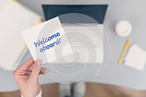 Woman clerk sitting holding note paper sticker with welcome aboard phrase. Business concept.