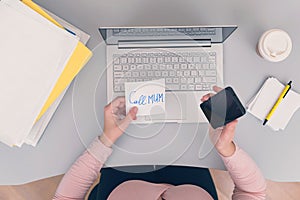 Woman clerk is sitting at office table holding note sticker with message call mum