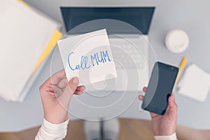 Woman clerk is sitting at office table holding note sticker with message call mum