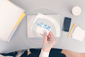 Woman clerk is sitting at office table holding note sticker with message call mum