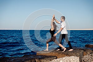 Woman client doing stretching or yoga outdoors background sea, personal trainer man correct her