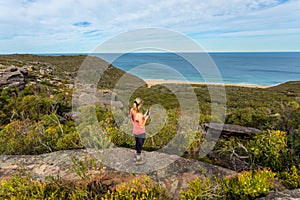Woman on clifftop holding mobile phone, views to ocean beach