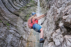 Woman climber on via ferrata next to waterfall, in Italy, Europe. Summer adventure extreme activities