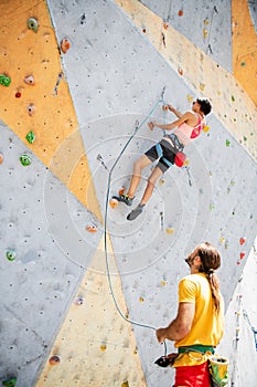 A woman climbing on climbing wall, belayed by male instructor
