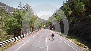 Woman climbing uphill in mountain on road bicycle. Endurance cycling workout. Professional cyclist training on bike outdoors. Tria