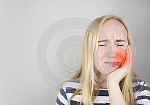 A woman clings to his cheek and winces in pain in his tooth. The concept of dental problems, caries, tooth decay, flux. White