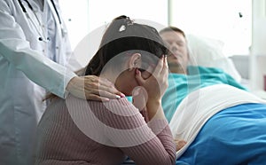 Woman in clinic crying near man in hospital bed