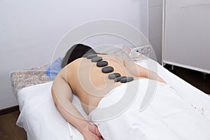 A woman in a clinic receiving hot stone massage. Back view