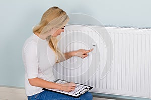 Woman With Clipboard Checking Digital Thermostat