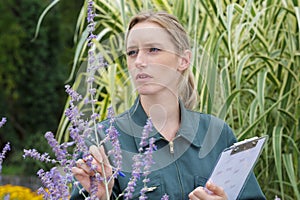 Woman with clipboard and pen writing and examining plants