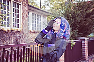 Woman in cloak and scarf on the head front of fence