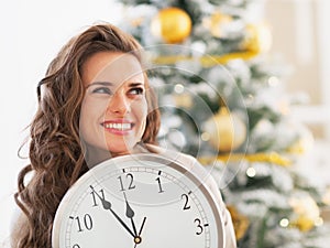 Woman with clock looking on copy space in frontof christmas tree