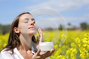 Woman applying moisturizer cream on cheek a sunny day photo