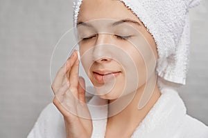 Woman with closed eyes applying moisturizer on face.