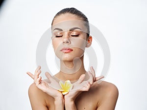 woman with closed eyes holding a yellow flower in her hands clean skin light background
