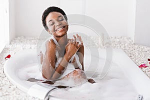 Woman with closed eyes of pleasure taking bath with foam and petals at home