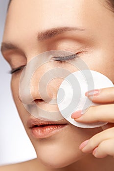 Woman with closed eyes taking off makeup with cotton wipe sponge cleansing face.