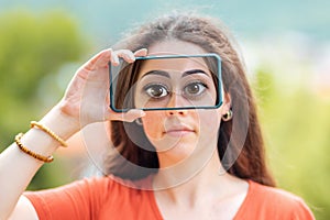 A woman closes her eyes with a smartphone, with a picture of huge cartoon eyes. The concept of hiding identity and fake pages in