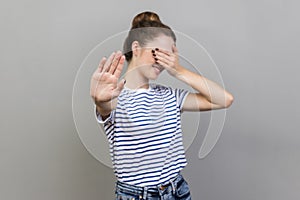 Woman closing eyes with palm and showing stop hand gesture, turning face, does not want to see.