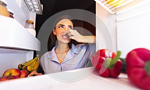 Woman closing nose near refrigerator, feeling bad smell