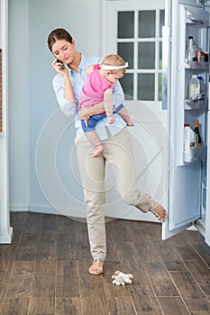 Woman closing refrigerator door while carrying baby girl