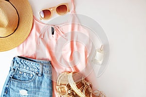 Woman clothes and accessories: pink top, jeans skirt, perfume, sandals, sunglasses, hat, lipstick on white background. Flat lay tr