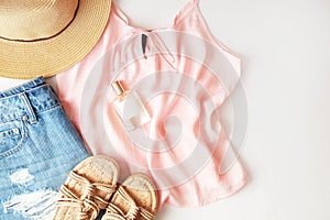 Woman clothes and accessories: pink top, jeans skirt, perfume, sandals, sunglasses, hat, lipstick on white background. Flat lay tr