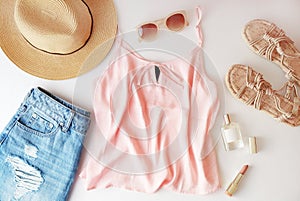 Woman clothes and accessories: pink top, jeans skirt, perfume, sandals, sunglasses, hat, lipstick on white background. Flat lay tr