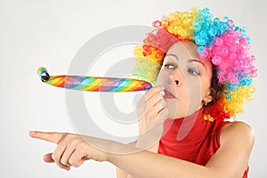 Woman in clown wig and party blower pointing left