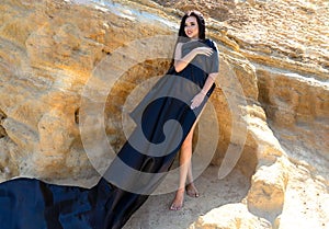 Woman on the coast, sea. long-haired brunette woman in a black dress near the stone