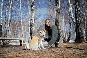 Woman in coat and an Akita Inu puppy in a winter birch park look at the camera