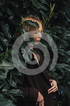 A woman in a coat on a background of green foliage. Stylish middle-aged woman, forty years old. Skinny physique