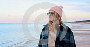 woman in coat and beanie hat enjoying walk on beach on chilly spring day