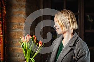 Woman in a coat with a bouquet of tulips on a dark background. Holiday, gift