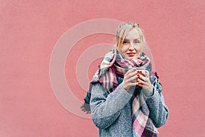 Woman in coat and scarf outside in winter with a mug with a drink.