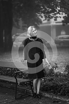 A woman in a coat stands near a park bench. Black and white photo.