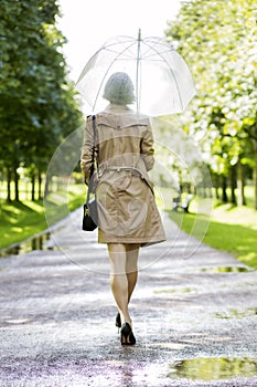 Woman at coat under umbrella walk in park