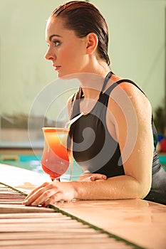 Woman with cocktail drink at swimming pool edge.