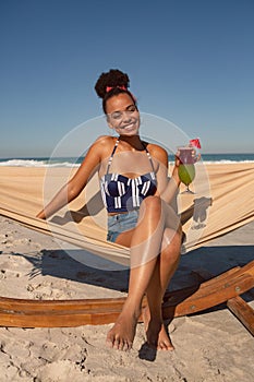 Woman with cocktail glass sitting on hammock at beach in the sunshine