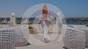 Woman is with a cocktail on a terrace. Girl from the back.