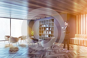 Woman with coffee in gray living room corner with bookcase