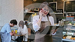 Woman coffee shop worker with clipboard talking on phone accepts confirms discusses order