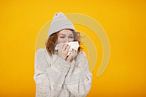 Woman with a cold blowing her runny nose with tissue. Portrait of beautiful girl in winter sweater and hat get sick sneezing from