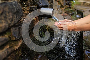 Woman collect pure water in hand palm from the source in the wall, hold and drink it. Female hand scooping spring water from the