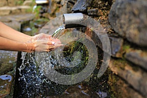 Woman collect pure water in hand palm from the source in the wall, hold and drink it. Female hand scooping spring water from the