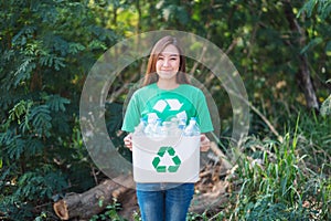 A woman collecting garbage and holding a recycle bin with plastic bottles in the outdoors